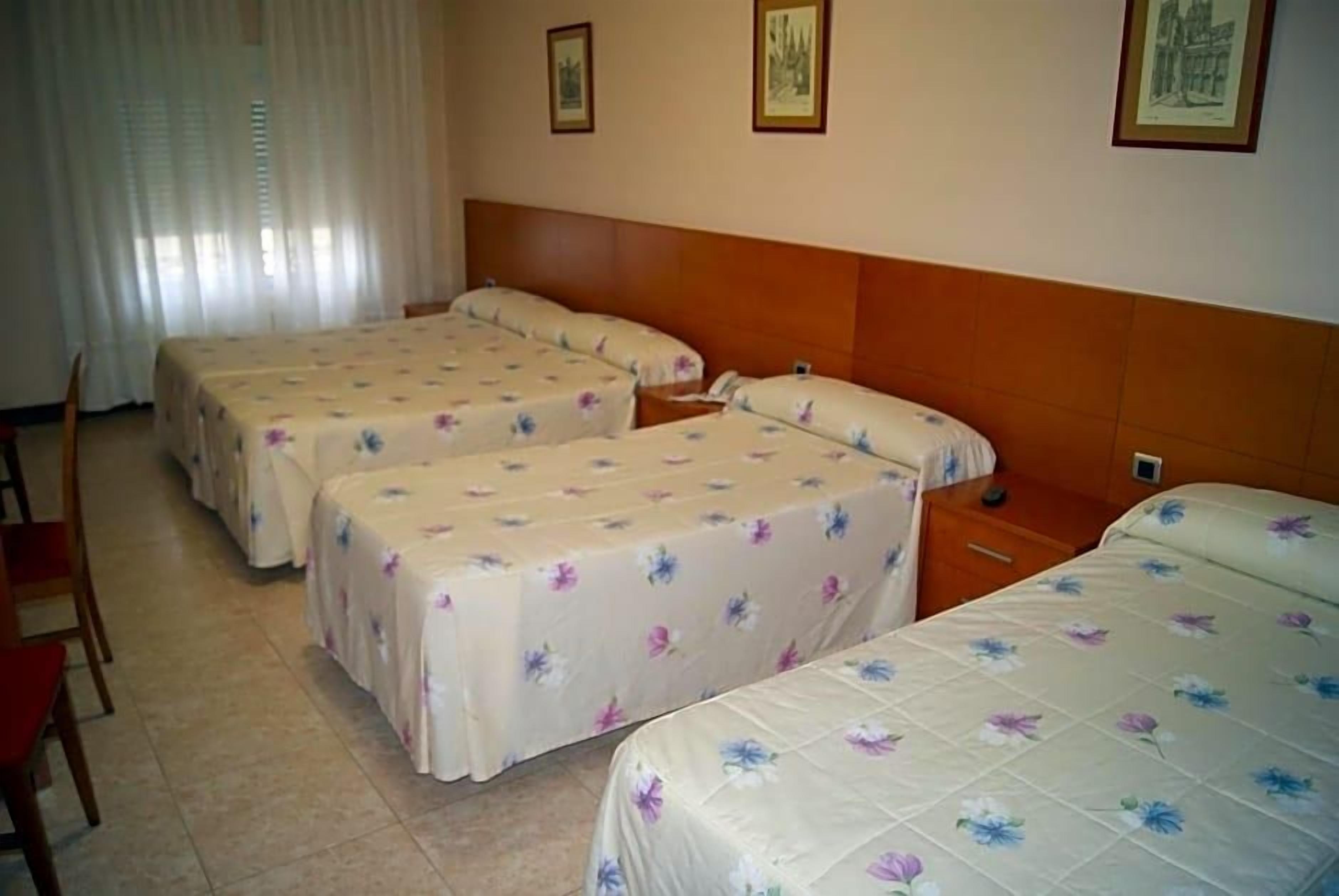 A hotel room with three beds, a wooden headboard, and a chair.