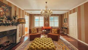 Een ruime woonkamer met een open haard, een kroonluchter, twee fauteuils, een kamerbreed tapijt en gestreepte wanden.