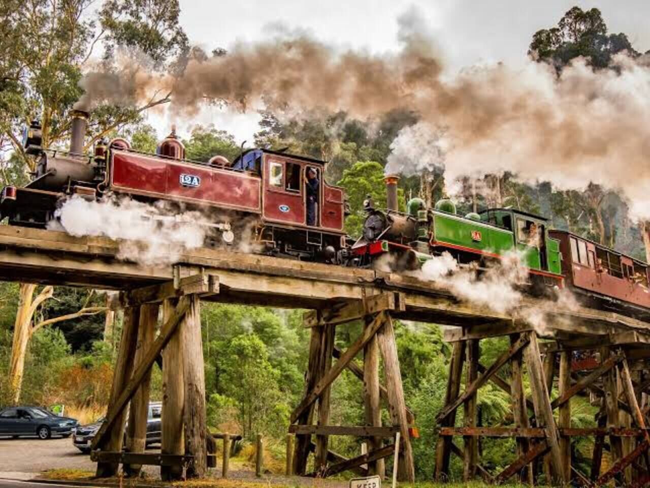 Un tren de vapor sobre un puente de madera, con humo y rodeado de vegetación.