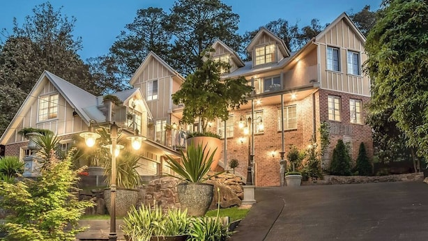 A large, multi-story house with a brick facade, multiple windows, and a well-maintained garden with various plants and a stone pathway.