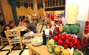 A dining area with tables and chairs, a buffet with various food items, and a decorative centerpiece. - Grand Makadi (Makadi Bay)