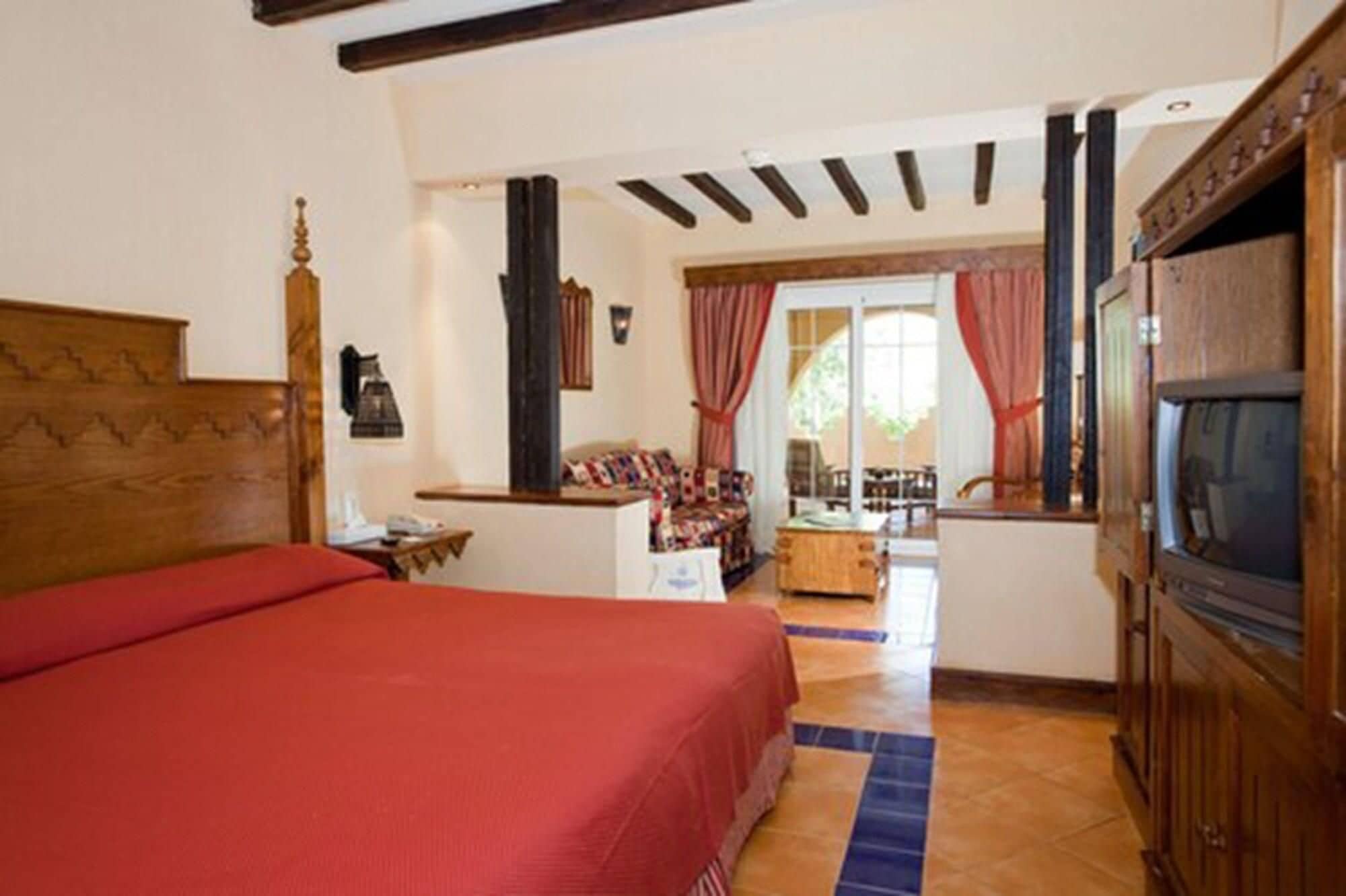 A room with a bed, a TV, a desk, and a view of the outside.