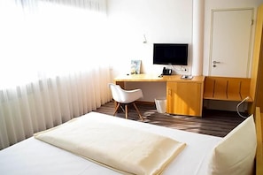 Habitación de hotel con una cama, un escritorio con computadora, una silla y un televisor.