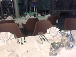 A restaurant with tables set for dining, including wine glasses, forks, and a pig-shaped salt shaker. - Cristall (Waghaeusel)
