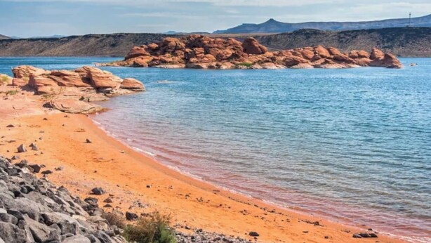 A beach with clear water, rocky formations, and distant mountains.