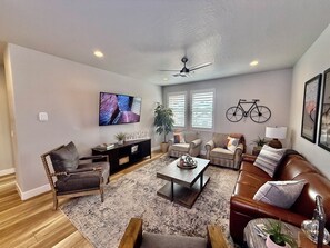 A living room with a flat-screen TV, a ceiling fan, a sofa, a coffee table, and a bicycle mounted on the wall.