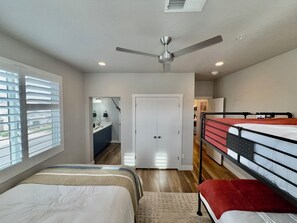A bedroom with bunk beds, a ceiling fan, a bathroom with a mirror and sink, and a door leading to another room.