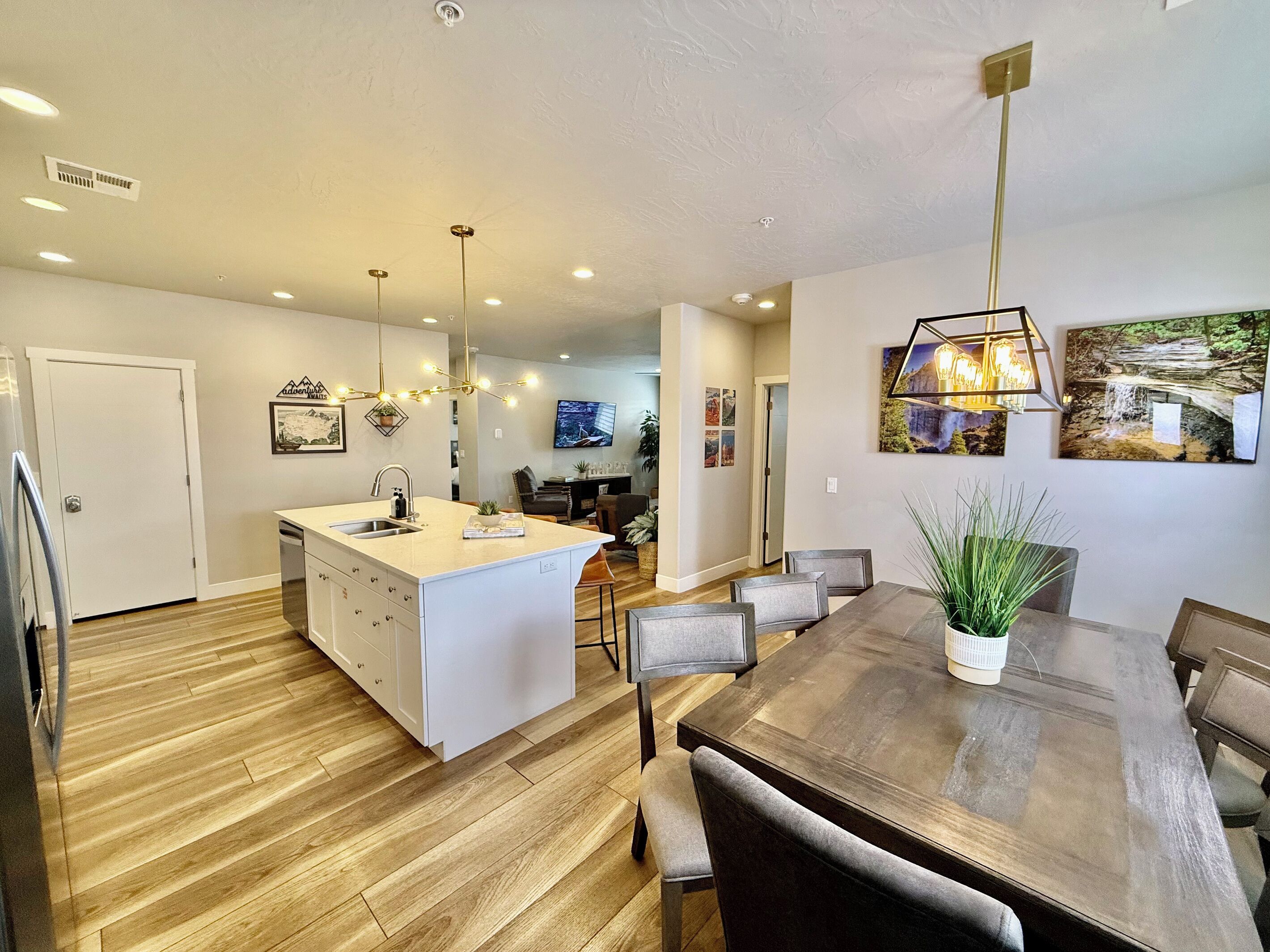 A modern kitchen with a central island, wooden flooring, and contemporary lighting fixtures.