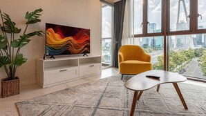 Una sala de estar moderna con vistas a la ciudad, un sillón amarillo, un televisor sobre un mueble blanco y un ventanal grande.