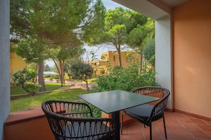 Uma varanda com mesa e cadeiras, com vista para um jardim e edifícios.