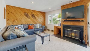 Ein Wohnzimmer mit einer Couch, einem Couchtisch, einem Kamin und einem an der Wand befestigten Fernseher.