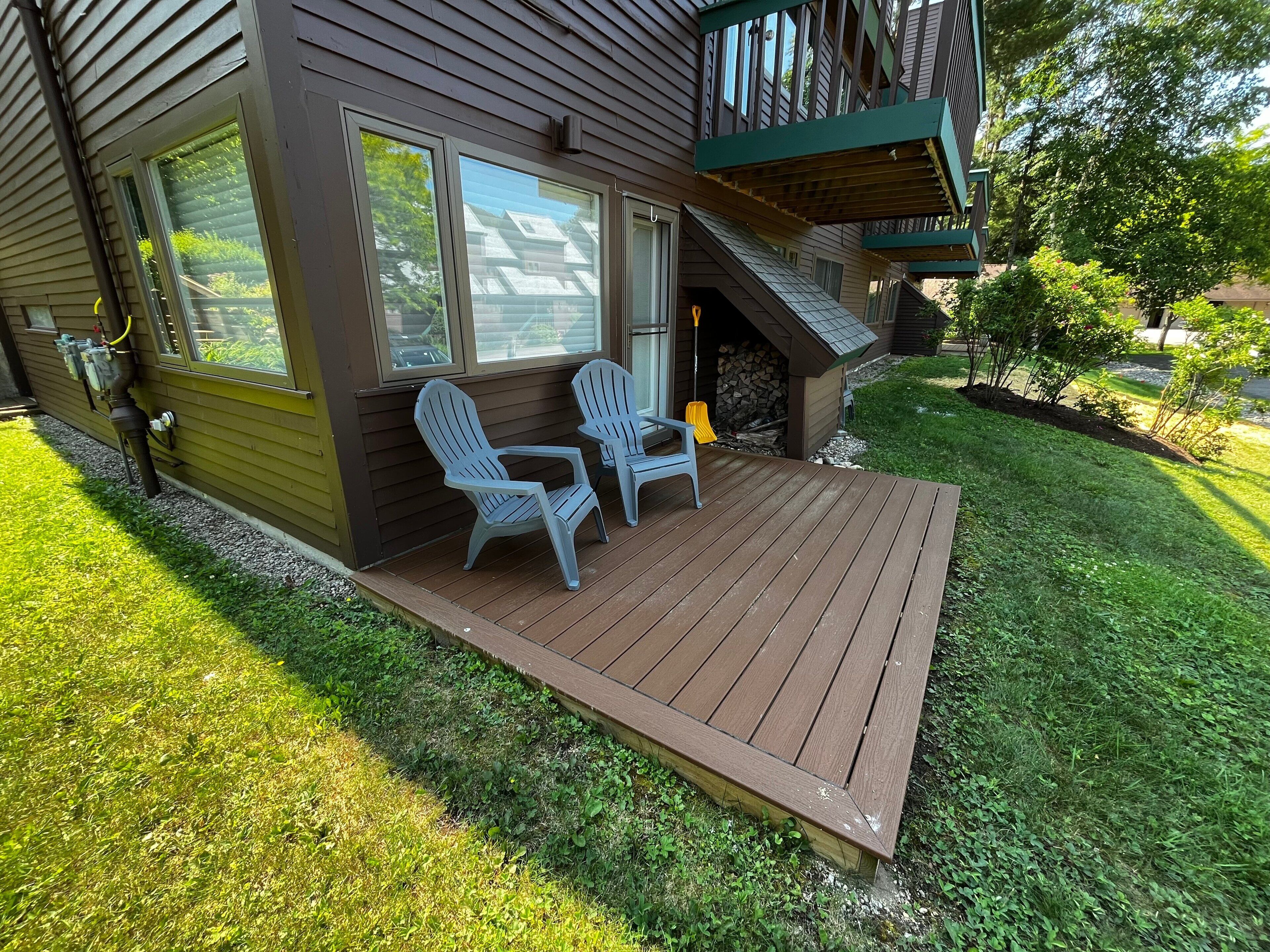 Una terraza con dos sillas Adirondack, un pozo de fuego y una escalera de madera que lleva a otra terraza.