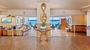 A lobby with a reception desk, a decorative infinity sculpture, a potted plant, and a view of the ocean. - High-Rise Paradise with Sweeping Ocean Views (Lahaina)