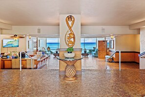 A lobby with a reception desk, a decorative infinity sculpture, a potted plant, and a view of the ocean. - High-Rise Paradise with Sweeping Ocean Views (Lahaina)