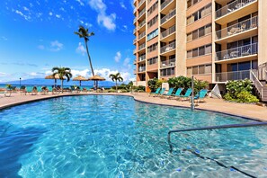 A swimming pool with clear blue water, surrounded by lounge chairs and palm trees. - High-Rise Paradise with Sweeping Ocean Views (Lahaina)