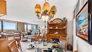 A dining area with a round glass table, wicker chairs, and a chandelier. - High-Rise Paradise with Sweeping Ocean Views (Lahaina)