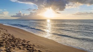 A beach with footprints, a clear sky, and a distant sailboat. - High-Rise Paradise with Sweeping Ocean Views (Lahaina)