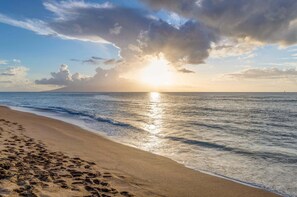 A beach with footprints, a clear sky, and a distant sailboat. - High-Rise Paradise with Sweeping Ocean Views (Lahaina)
