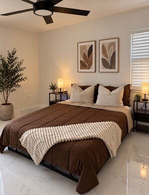 A bedroom with a bed, a ceiling fan, two wall-mounted lamps, a potted plant, and framed artwork. - Central House Stadium+Airport - Busch Gardens 3BR BBQ 7 PPL Tampa FL (Tampa)