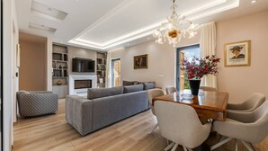 A modern living room with a sofa, dining table, and chairs, a TV, and a chandelier. - Villa Morava No 74 Belvedere Kor a (Qendër Bulgarec)