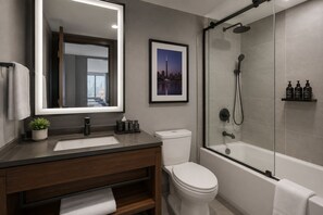A modern bathroom with a large mirror, a framed cityscape picture, a glass-enclosed shower, and a white toilet. - Modern Apartments (Toronto)