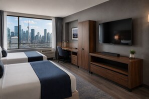 A hotel room with two beds, a desk, a TV, and a city view. - Modern Apartments (Toronto)