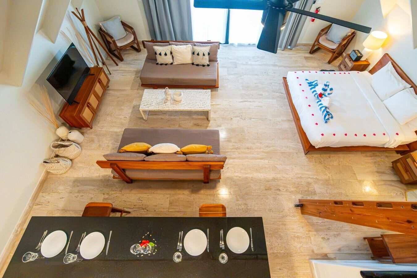 A hotel room with a sofa, a bed, a dining table set with plates and cutlery, a TV, and a lamp.