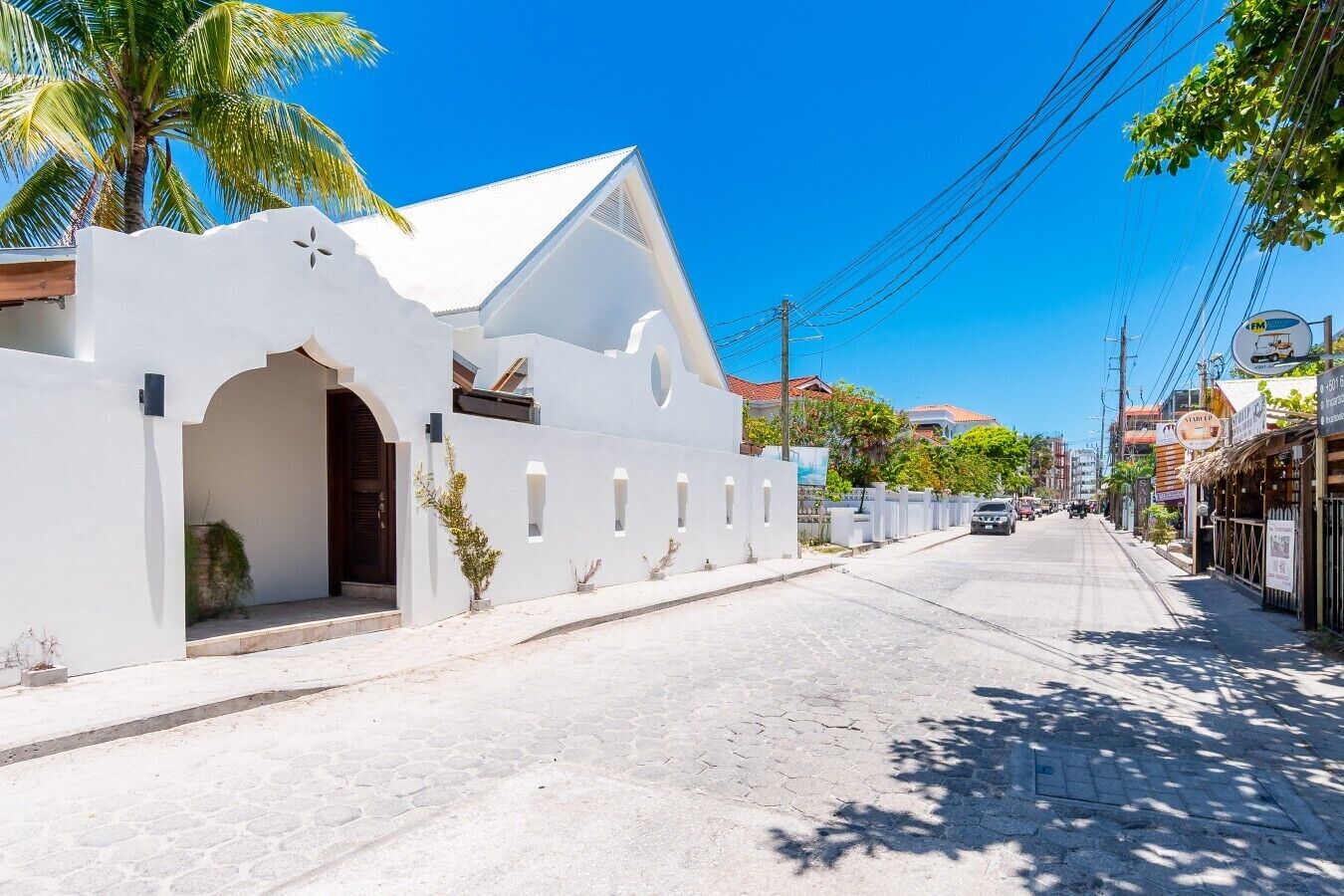 A street with a white building featuring an arched entrance and a sloped roof.