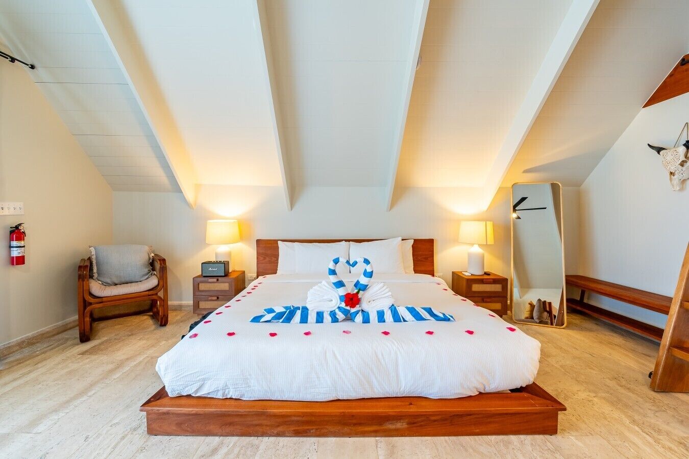Habitación de hotel con una cama grande, dos mesitas de noche, una silla, un espejo y un extintor.