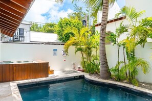 A swimming pool with a wooden deck and a hot tub, surrounded by tropical plants and a white wall. - The Annex - Private Villa - Large Pool and Jacuzzi (San Pedro)