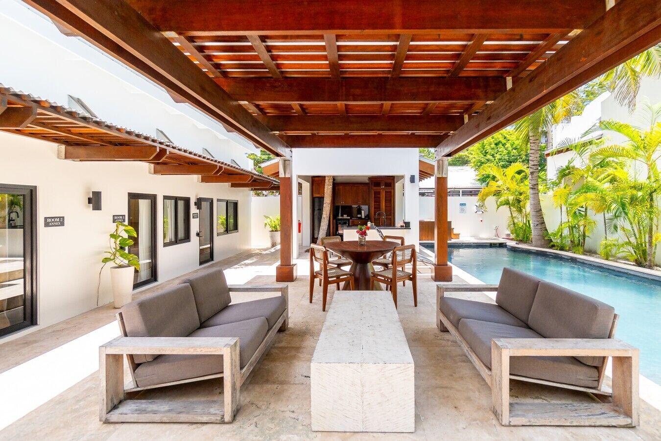A covered outdoor seating area with a pool, wooden furniture, and a view of the pool.