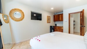 Ein Schlafzimmer mit Bett, Fernseher, Spiegel und einer Küchenzeile.