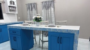 Een keuken met blauwe kastjes, een wit aanrechtblad en een eethoek met een tafel en stoelen.