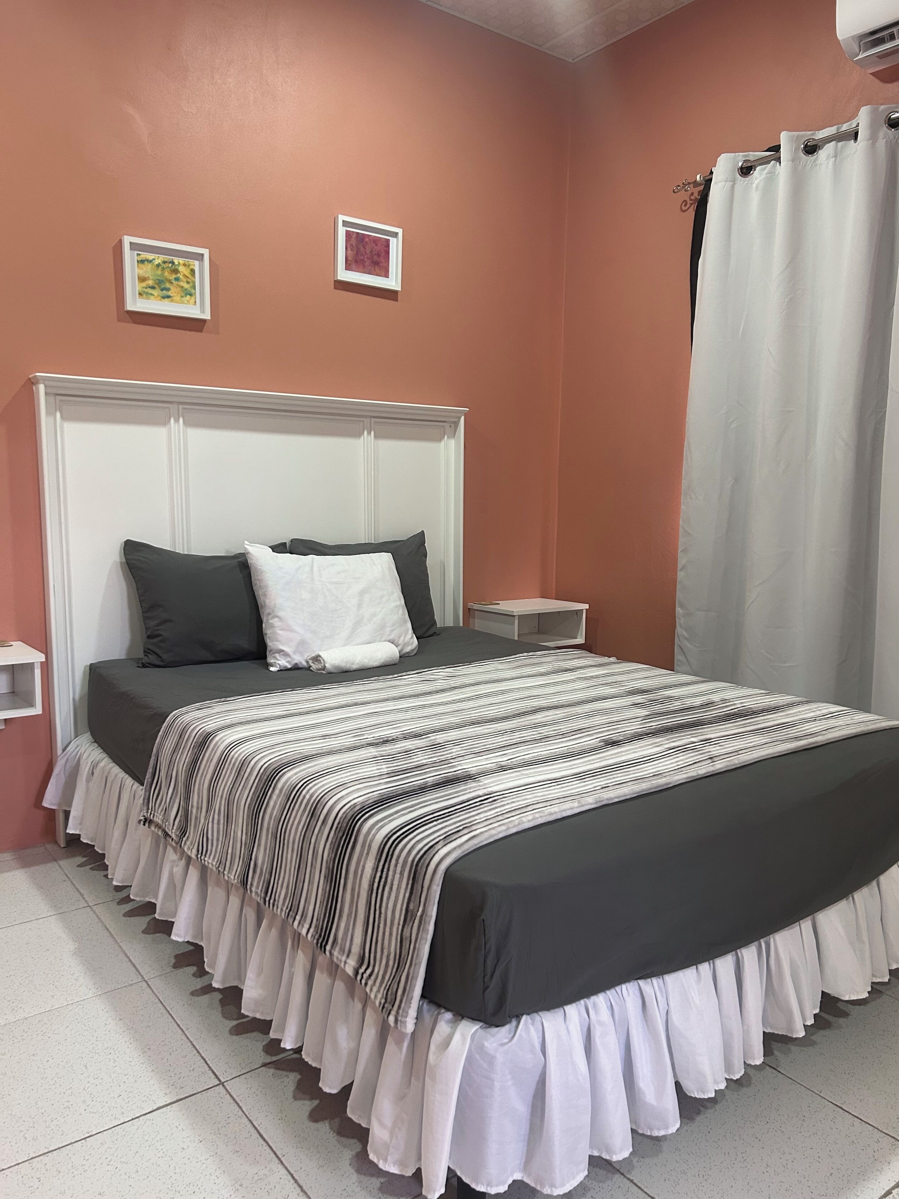A bedroom with a bed, a headboard, a nightstand, and a window with curtains.