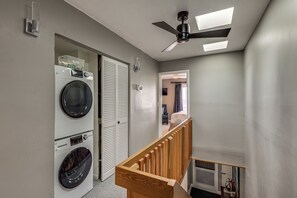 Ein Waschraum mit übereinander gestapelten Waschmaschinen und Trocknern, einem Deckenventilator und einer Holzgeländer.