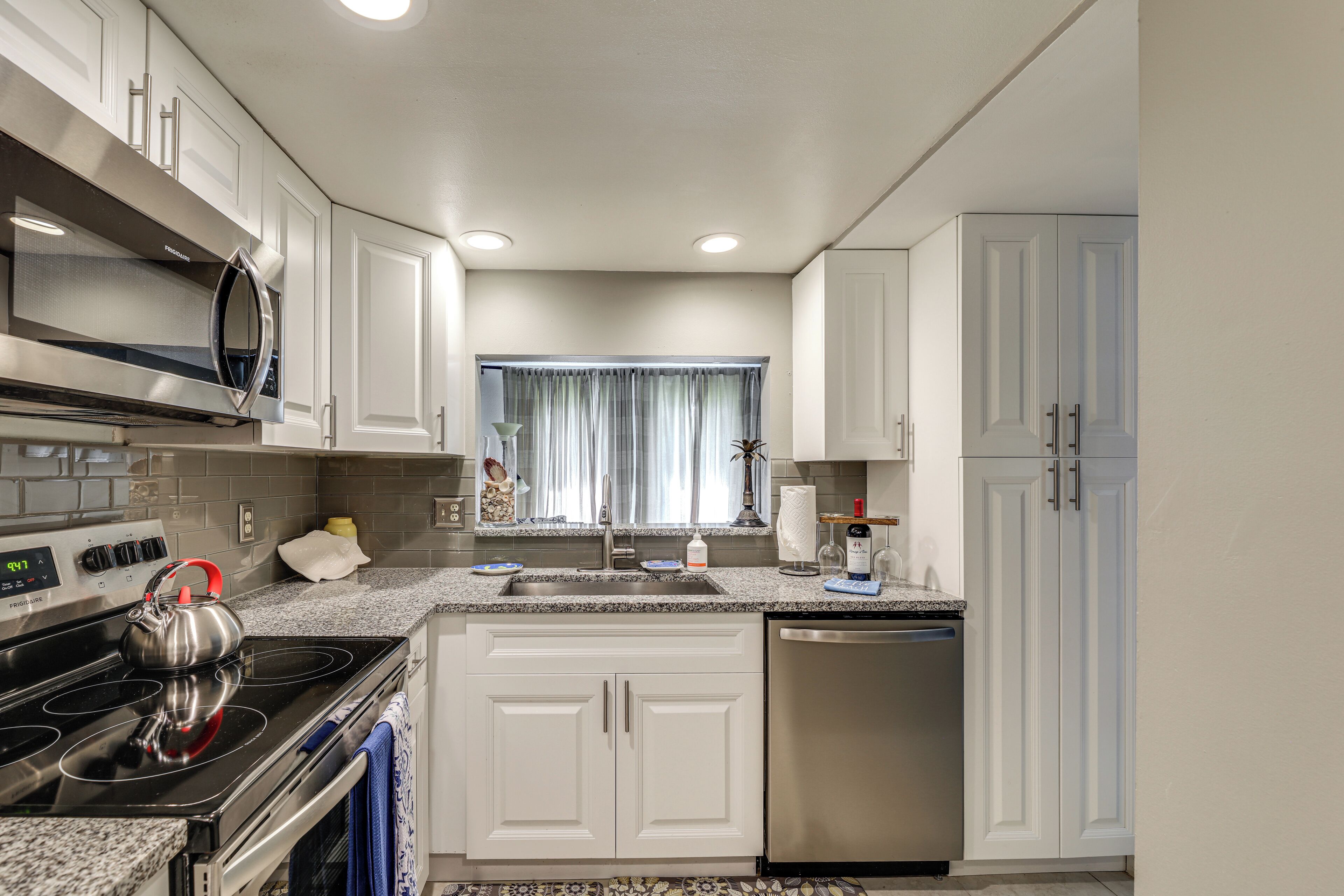 A modern kitchen with white cabinets, stainless steel appliances, and a window with curtains.