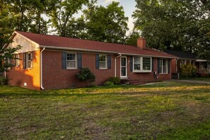 A single-story brick house with a gabled roof, a front porch, and a small front yard.