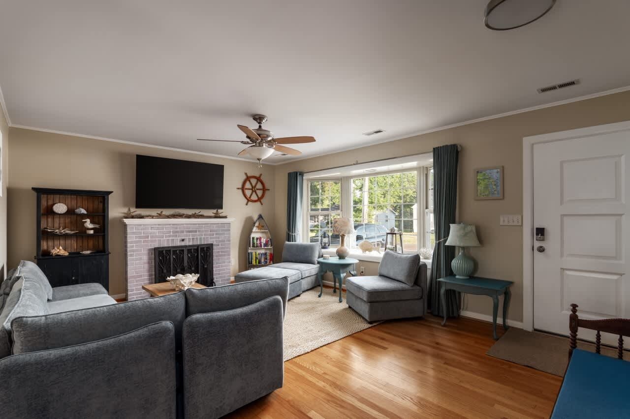 A living room with a fireplace, a ceiling fan, and a large window.