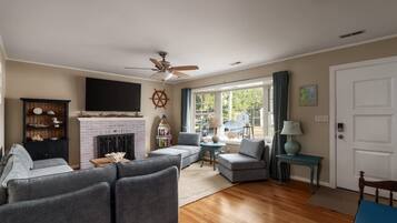 A living room with a fireplace, a ceiling fan, and a large window.