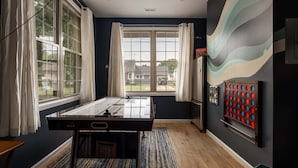 Quarto com mesa de futebol de mesa, uma janela grande com cortinas, um jogo fixado na parede e vista para o exterior.