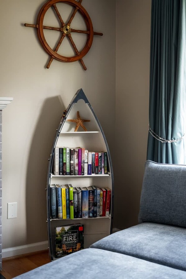 A bookshelf with books and a starfish decoration, a sailboat-shaped shelf, and a ship's wheel on the wall.