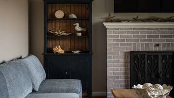 A living room with a grey sofa, a dark wooden bookcase with decorative items, and a brick fireplace with a decorative mantel.