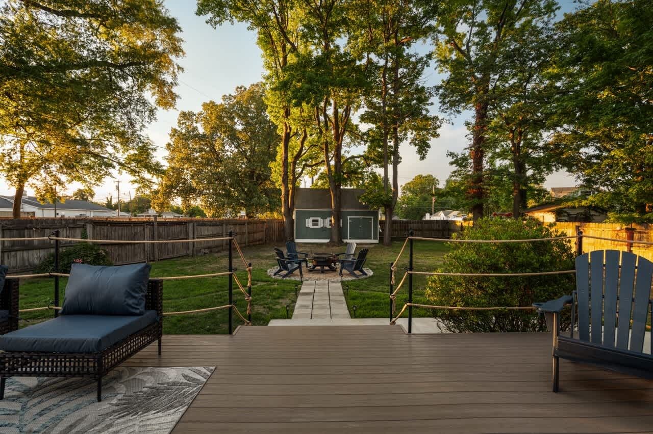 A deck with outdoor furniture, a small table, and a view of a house in the background.