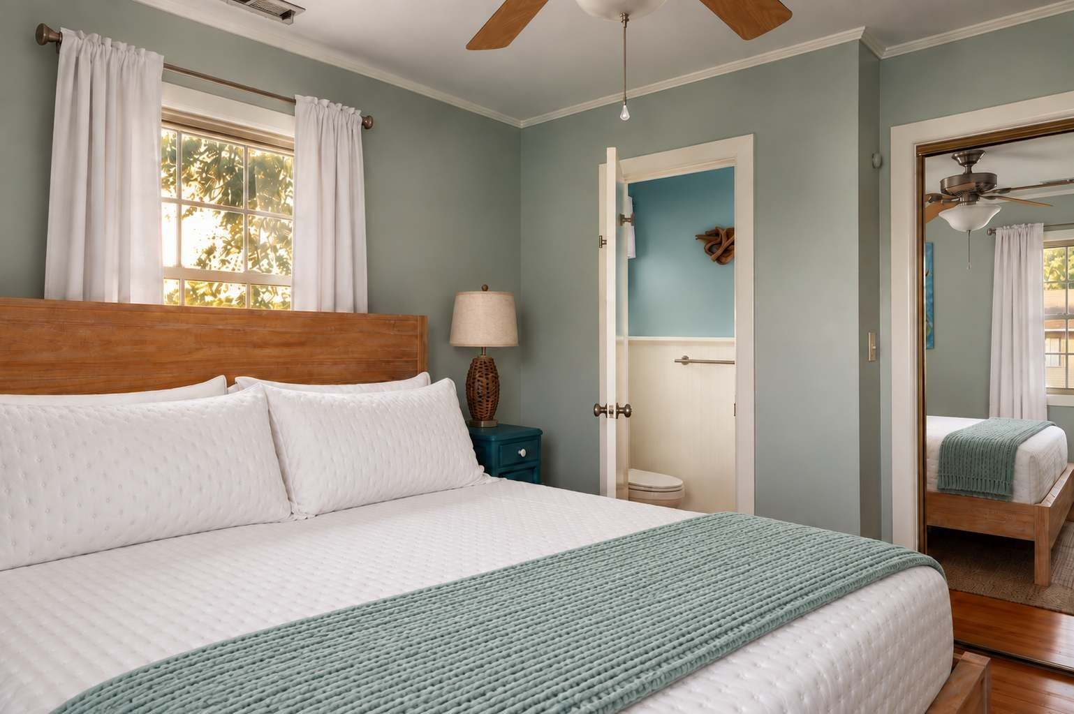 A bedroom with a large bed, a nightstand, a lamp, and a door leading to a bathroom.