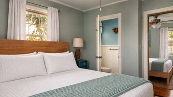 A bedroom with a large bed, a nightstand, a lamp, and a door leading to a bathroom.