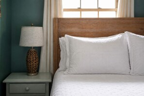 A bed with white bedding, a wooden headboard, and a bedside table with a lamp.