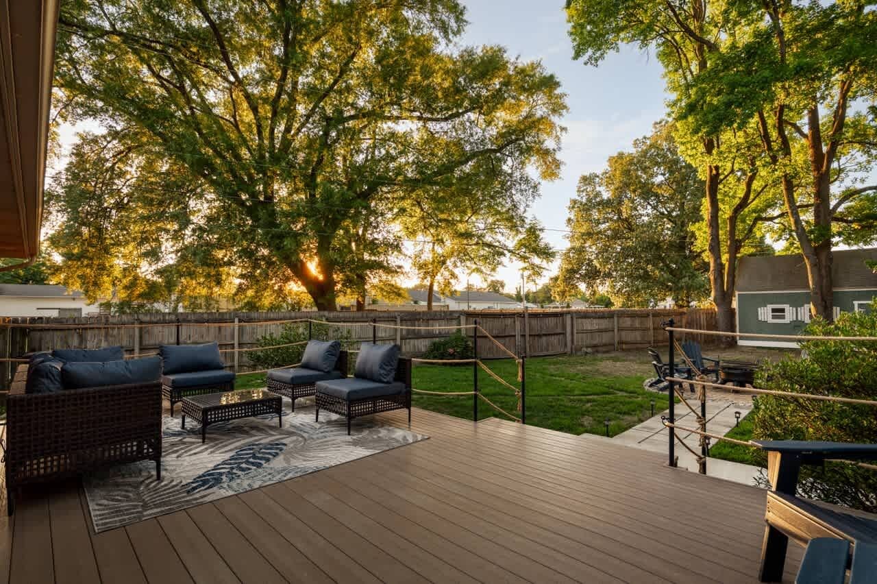 Una terraza con mobiliario exterior, una valla de madera y árboles al fondo.