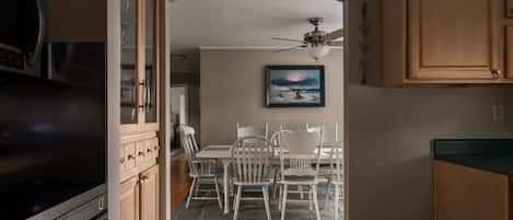 A kitchen with wooden cabinets, a refrigerator, and a dining area with white chairs and a table.