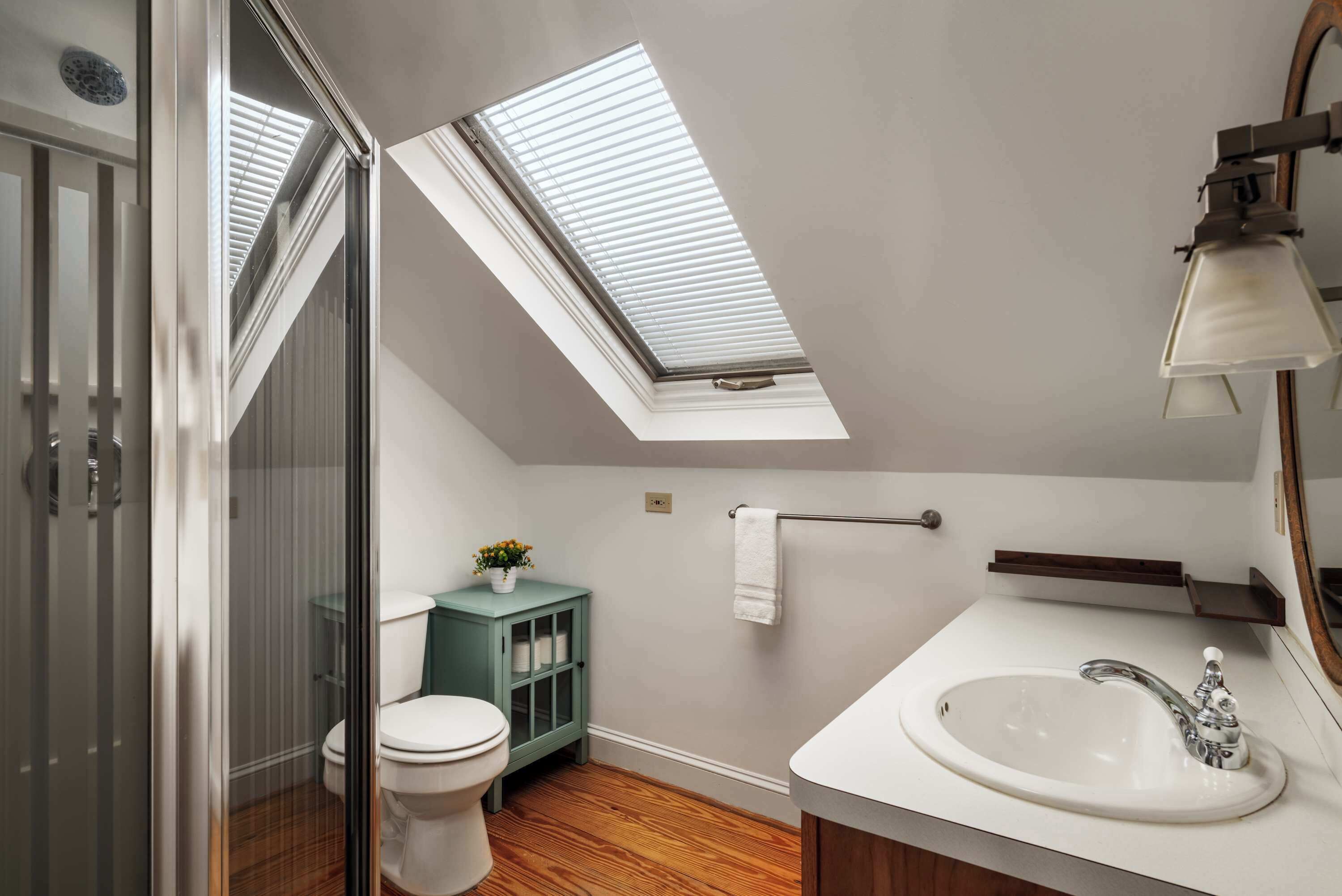 A bathroom with a skylight, a toilet, a cabinet, a sink, and a mirror.