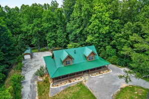 Eine Lodge mit einem grünen Dach, einer Holzwandfassade und einer Veranda mit Sitzgelegenheiten.